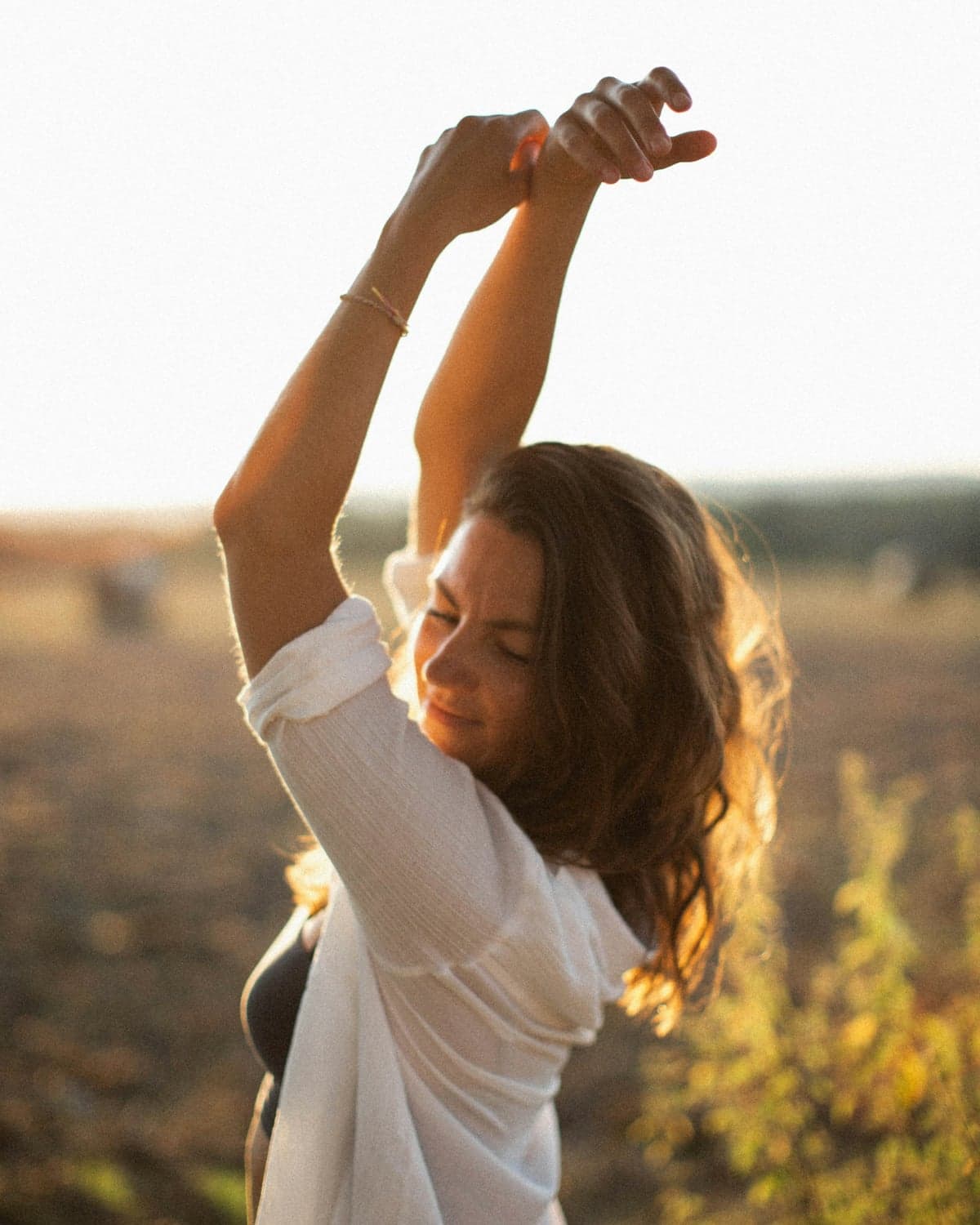 A woman stretching her arms overhead in an open field at sunset