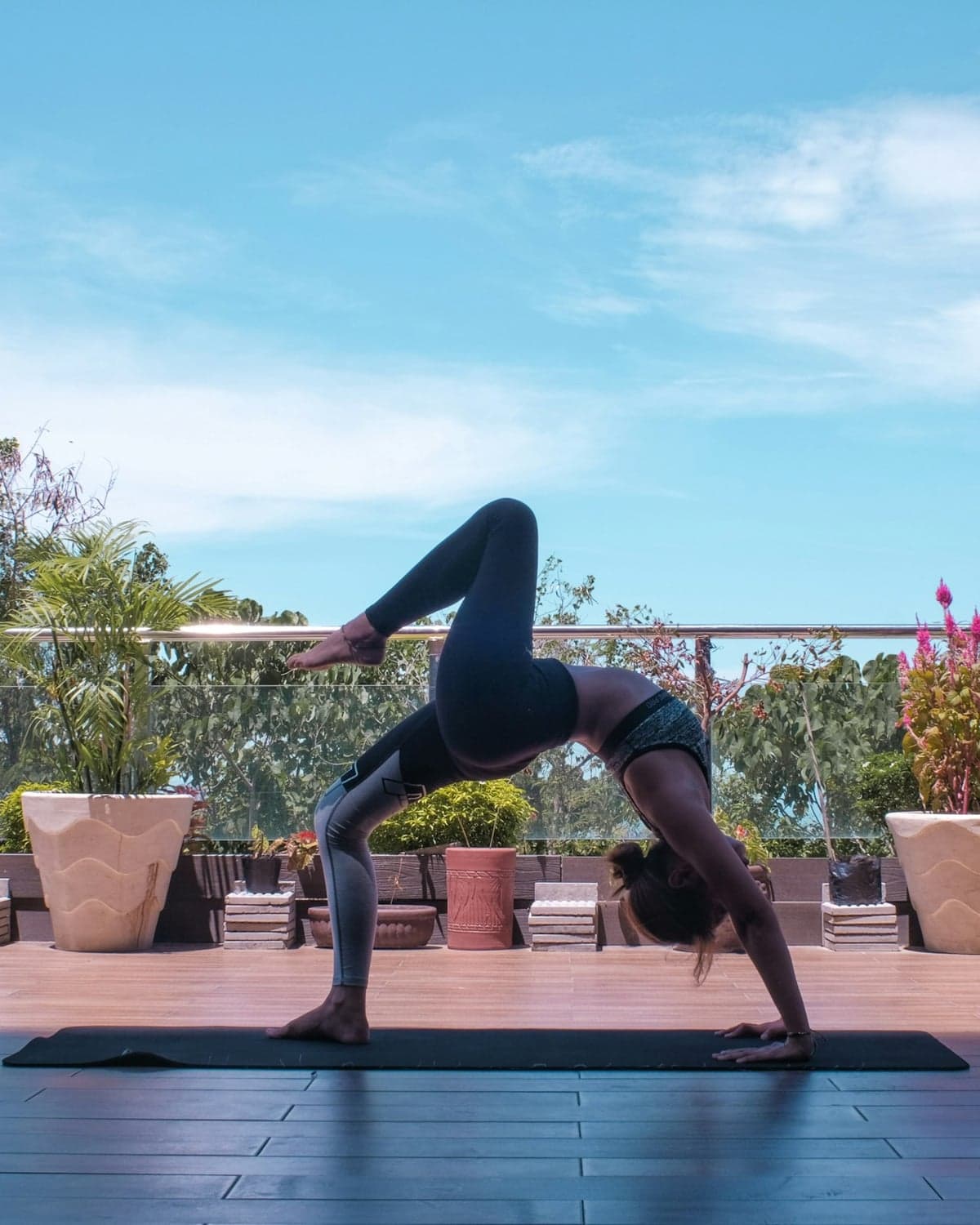 A woman holding a backbend stretch on a sunlit outdoor terrace